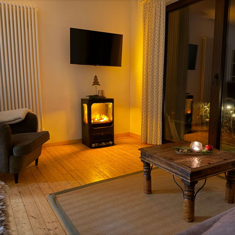 Blick von der Couch auf das stimmungsvolle Flammenspiel des Elektrokamins in der Ferienwohnung Eifelcottage auf dem Landgut Pfauenhof in der Eifel.