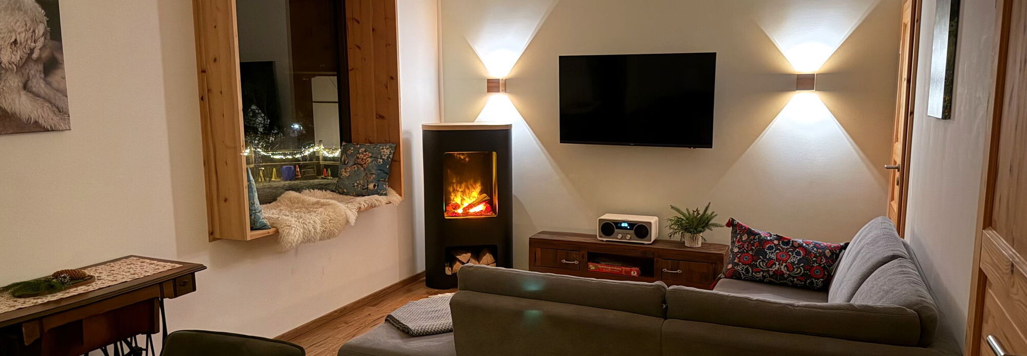 Das Wohnzimmer mit dem stimmungsvollen Flammenspiel des Elektrokamins im Ferienhaus Landchalet Eifel auf dem Landgut Pfauenhof in der Eifel.